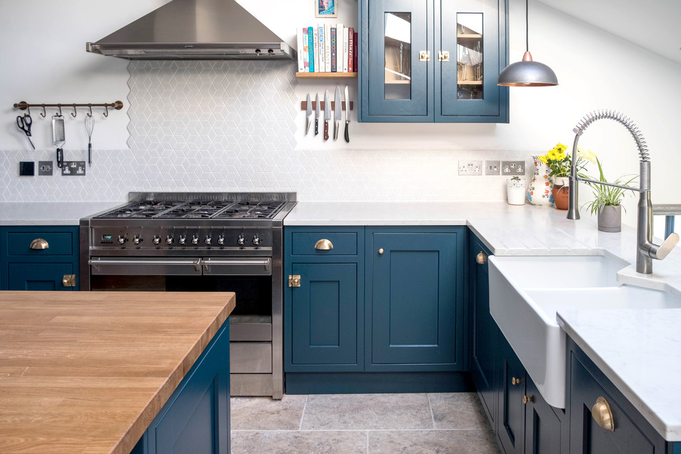 Mid-sized country u-shaped open plan kitchen in London with a farmhouse sink, shaker cabinets, blue cabinets, white splashback, porcelain splashback, stainless steel appliances, porcelain floors, with island, white benchtop, solid surface benchtops and grey floor.