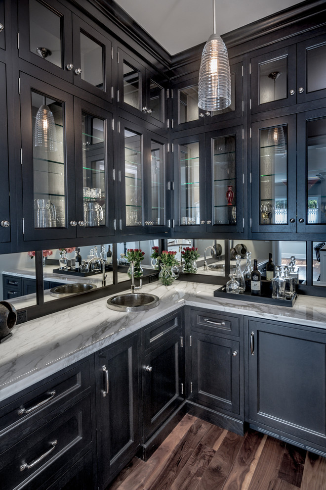 Photo of a large transitional l-shaped eat-in kitchen in St Louis with a drop-in sink, glass-front cabinets, black cabinets, marble benchtops, mirror splashback, panelled appliances, dark hardwood floors and with island.