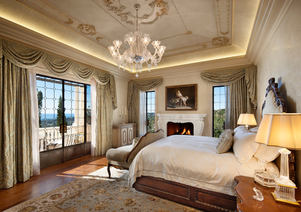 Photo of a mediterranean bedroom in Santa Barbara with beige walls, medium hardwood floors and a standard fireplace.
