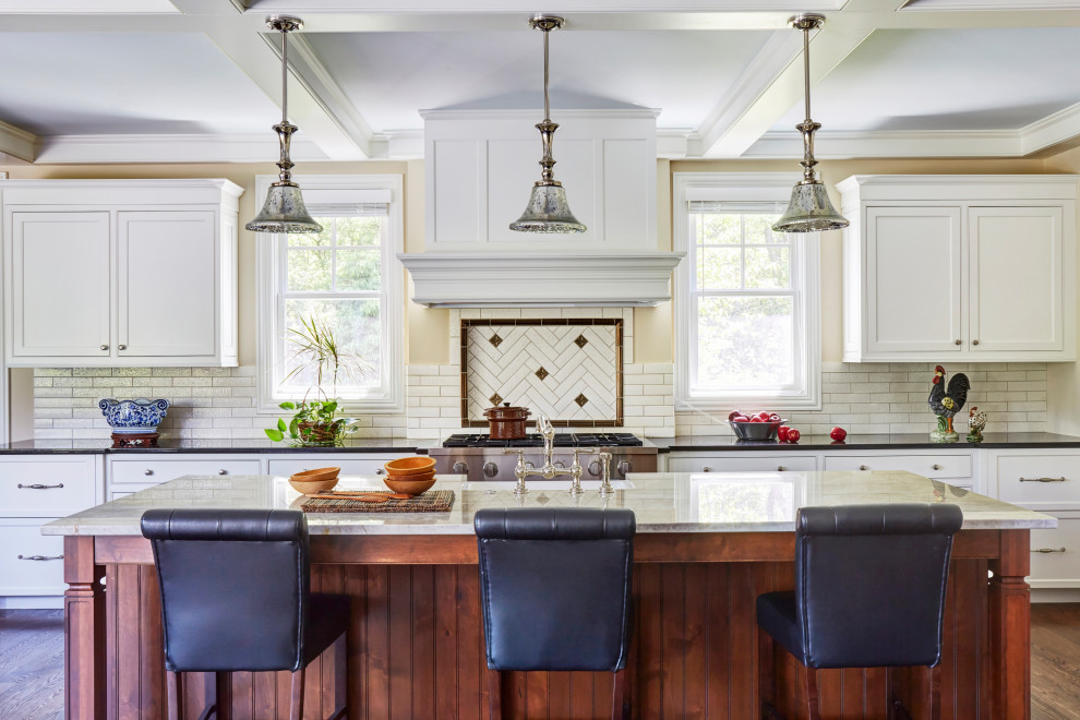 Design ideas for a large traditional u-shaped open plan kitchen in Chicago with a farmhouse sink, shaker cabinets, white cabinets, granite benchtops, white splashback, ceramic splashback, stainless steel appliances, medium hardwood floors, with island, brown floor, black benchtop and coffered.