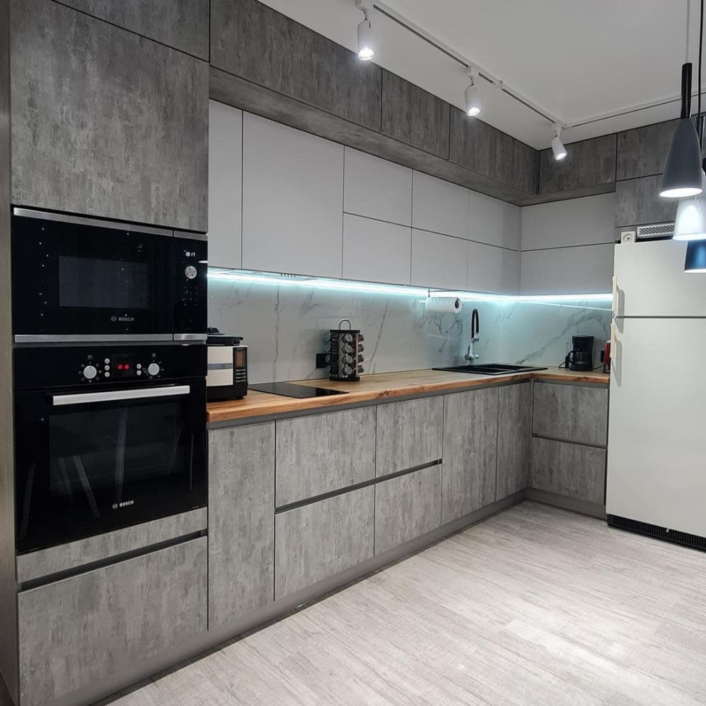 This is an example of a mid-sized contemporary l-shaped eat-in kitchen in Moscow with a drop-in sink, flat-panel cabinets, grey cabinets, wood benchtops, white splashback, granite splashback, black appliances, laminate floors, no island, grey floor and brown benchtop.