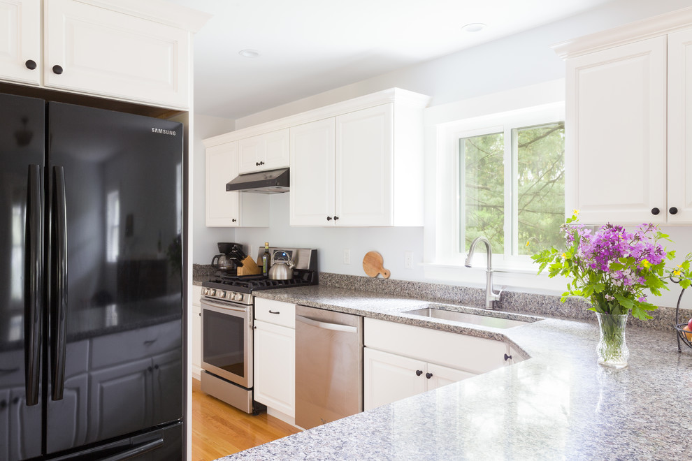Design ideas for a mid-sized traditional l-shaped eat-in kitchen in Boston with an undermount sink, raised-panel cabinets, white cabinets, granite benchtops, stainless steel appliances, light hardwood floors, a peninsula and grey benchtop.