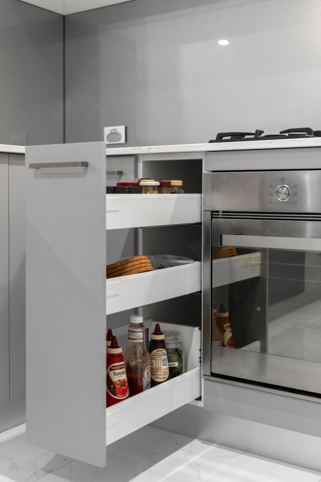 Photo of a large contemporary u-shaped eat-in kitchen in Perth with an undermount sink, shaker cabinets, grey cabinets, solid surface benchtops, grey splashback, glass sheet splashback, no island, white floor and white benchtop.