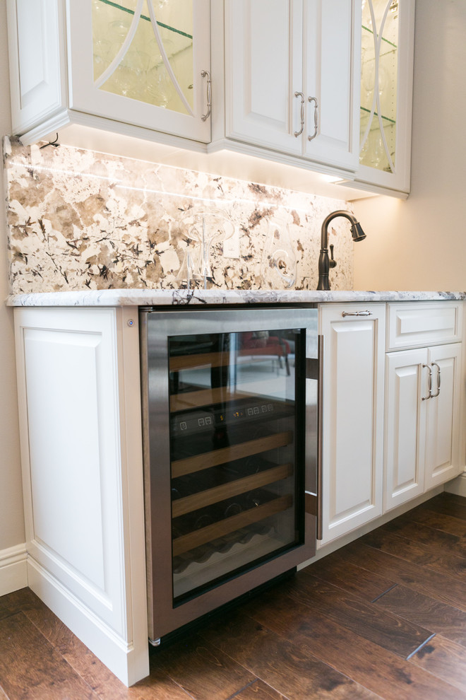 This is an example of a mid-sized transitional single-wall wet bar in Orlando with an undermount sink, white cabinets, granite benchtops, white splashback, medium hardwood floors, stone slab splashback, brown floor and raised-panel cabinets.