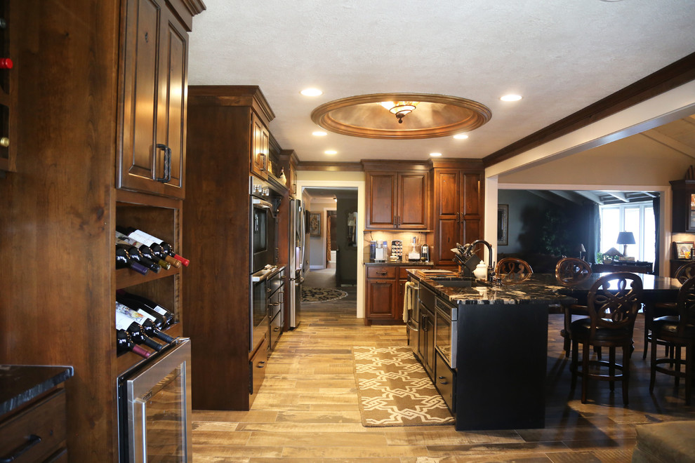 Mid-sized l-shaped porcelain tile eat-in kitchen photo with a double-bowl sink, raised-panel cabinets, medium tone wood cabinets, granite countertops, beige backsplash, cement tile backsplash, stainless steel appliances and an island