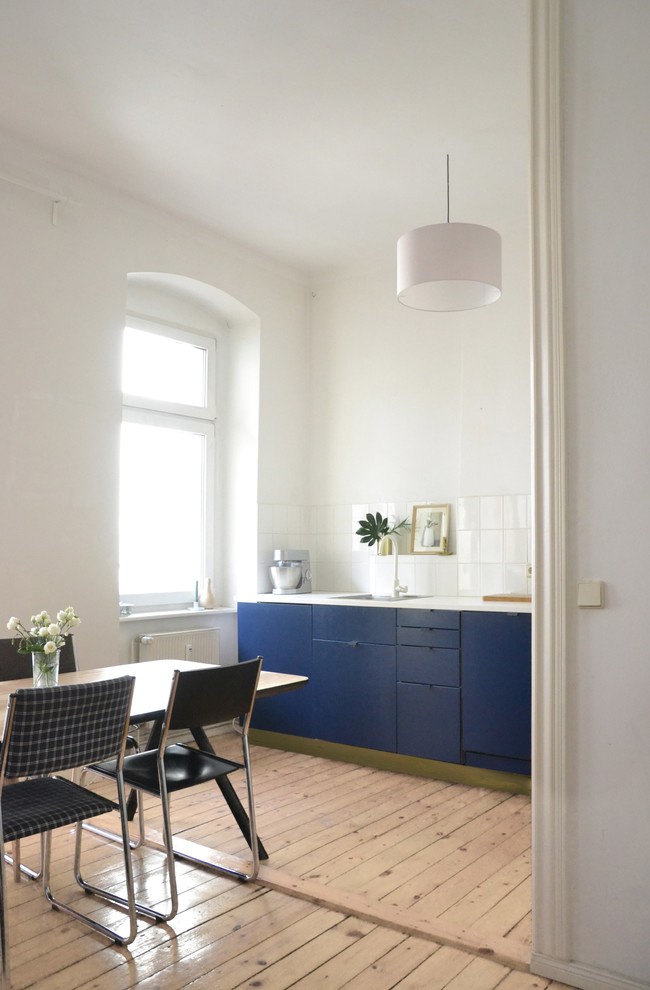 Small midcentury galley open plan kitchen in Berlin with a drop-in sink, flat-panel cabinets, blue cabinets, laminate benchtops, white splashback, panelled appliances, light hardwood floors, brown floor, ceramic splashback and no island.