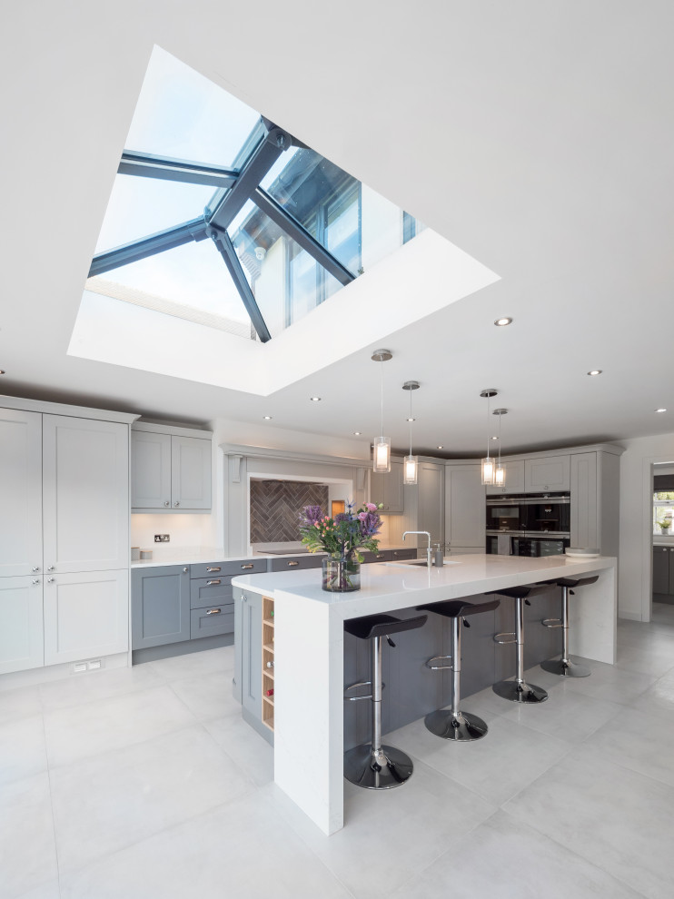 Design ideas for a large transitional l-shaped open plan kitchen in West Midlands with a drop-in sink, grey cabinets, marble benchtops, ceramic splashback, black appliances, ceramic floors, with island, grey floor, white benchtop, shaker cabinets and white splashback.