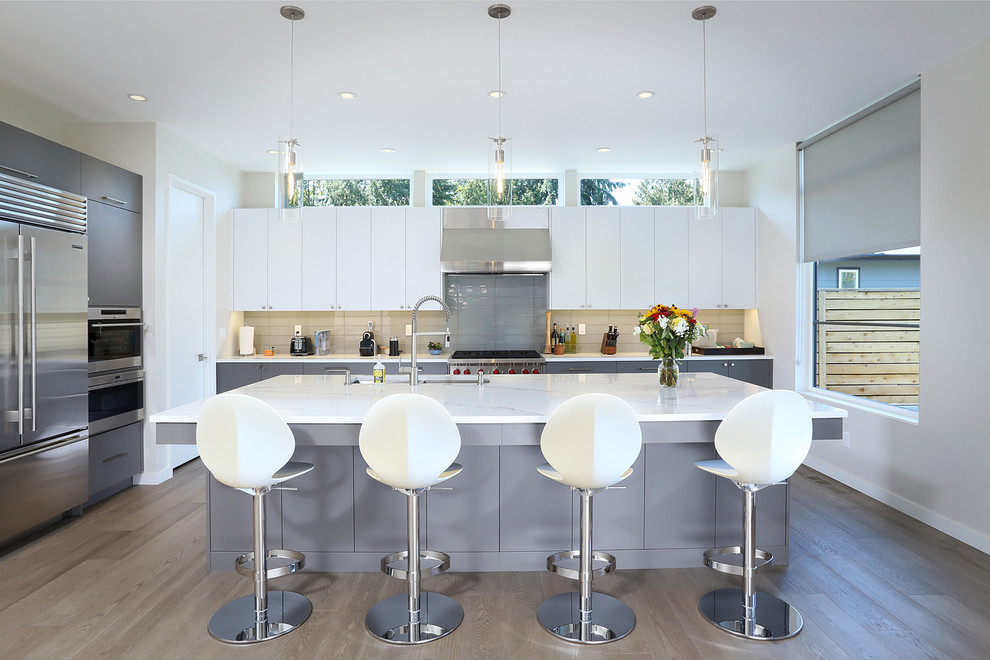 This is an example of a large contemporary l-shaped eat-in kitchen in Seattle with an undermount sink, flat-panel cabinets, grey cabinets, quartz benchtops, stainless steel appliances, medium hardwood floors, with island, beige splashback, grey floor and white benchtop.