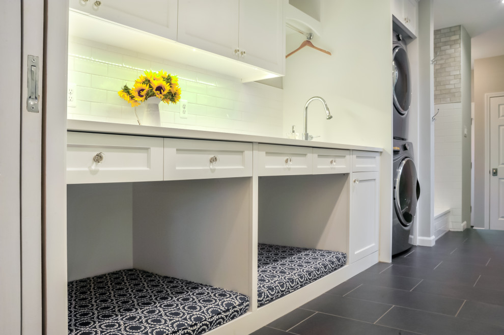 Photo of a small traditional galley utility room in Detroit with an undermount sink, shaker cabinets, white cabinets, quartz benchtops, white splashback, subway tile splashback, white walls, porcelain floors, a stacked washer and dryer, grey floor and white benchtop.
