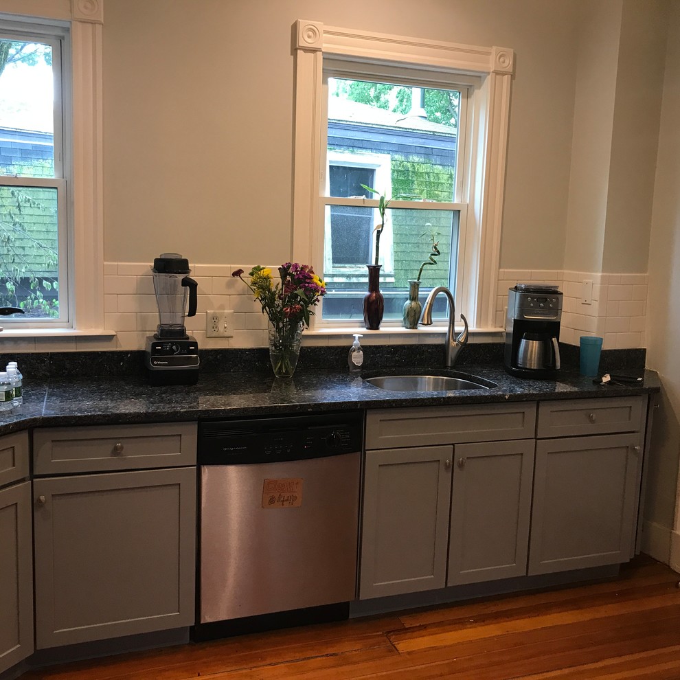 Mid-sized transitional l-shaped medium tone wood floor and brown floor enclosed kitchen photo with an undermount sink, shaker cabinets, gray cabinets, granite countertops, white backsplash, subway tile backsplash, no island and black countertops