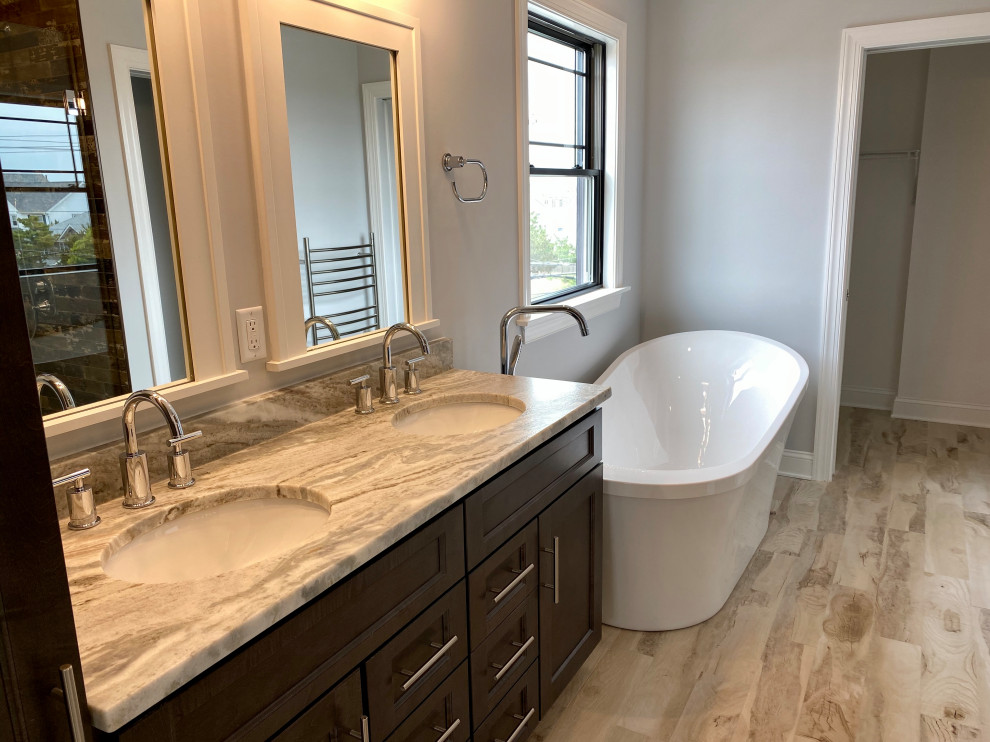 Photo of a mid-sized beach style master bathroom in New York with shaker cabinets, dark wood cabinets, a freestanding tub, an alcove shower, a two-piece toilet, gray tile, wood-look tile, grey walls, wood-look tile, an undermount sink, granite benchtops, beige floor, a hinged shower door, grey benchtops, a niche, a double vanity and a freestanding vanity.