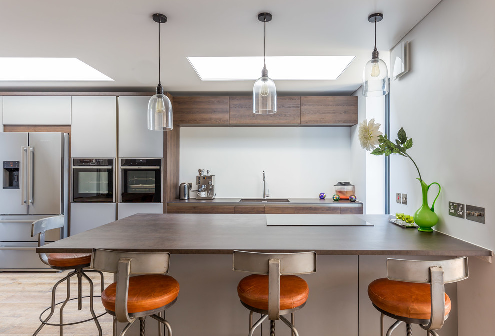 Contemporary kitchen in Sussex with flat-panel cabinets, dark wood cabinets, wood benchtops, white splashback, stainless steel appliances, light hardwood floors, brown floor, a double-bowl sink and a peninsula.