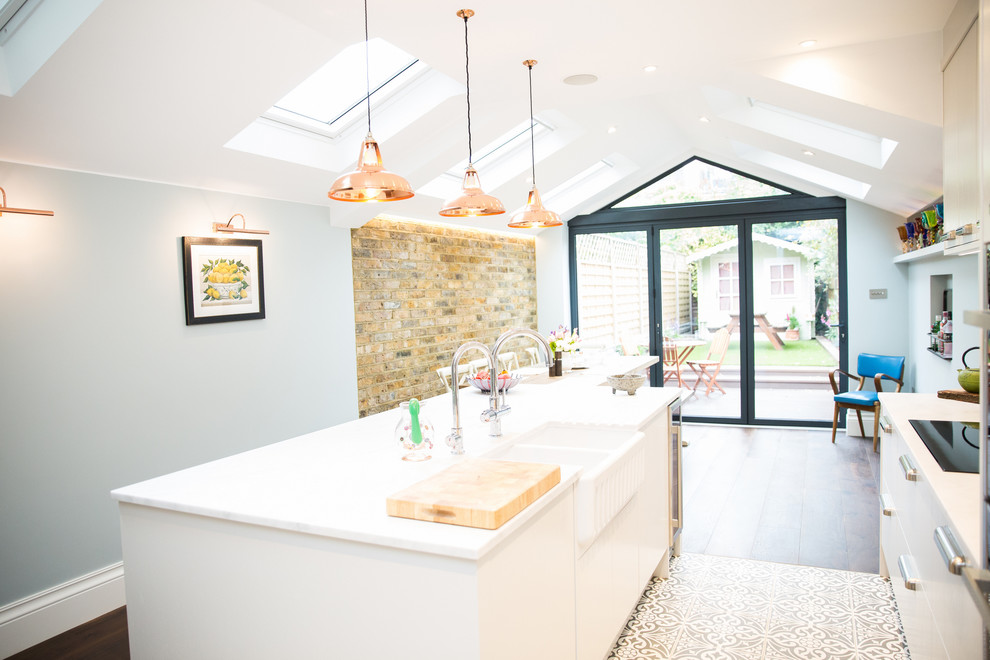 This is an example of a mid-sized eclectic galley eat-in kitchen in London with a farmhouse sink, flat-panel cabinets, white cabinets, with island, white benchtop, solid surface benchtops, ceramic floors and multi-coloured floor.