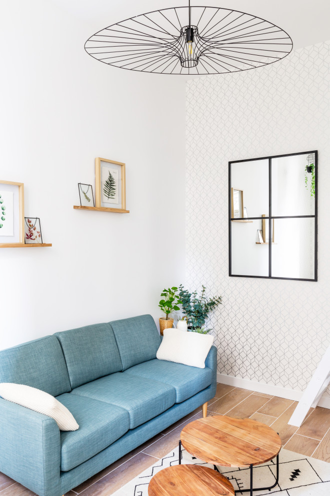 На фото: маленькая открытая гостиная комната в скандинавском стиле с с книжными шкафами и полками, серыми стенами, телевизором в углу, бежевым полом, потолком с обоями, обоями на стенах и синим диваном для на участке и в саду
