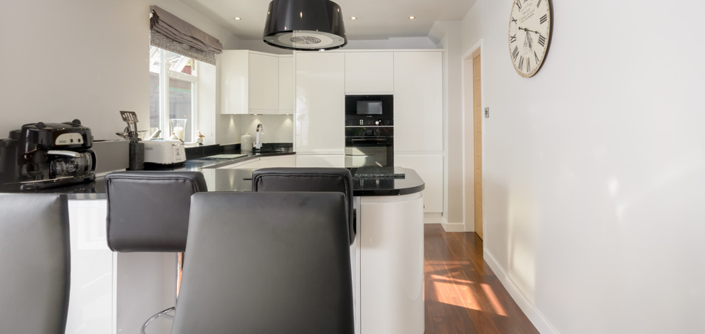 Photo of a small contemporary u-shaped eat-in kitchen in Other with white cabinets, solid surface benchtops and black appliances.