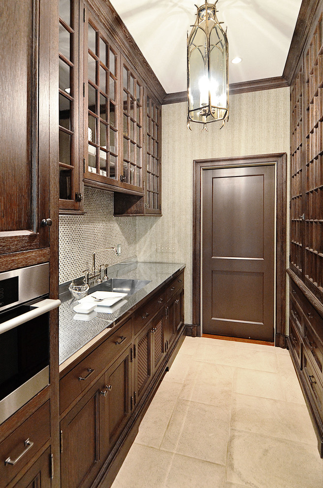 This is an example of a large traditional galley kitchen pantry in Other with glass-front cabinets, brown cabinets, mosaic tile splashback, stainless steel appliances, limestone floors, no island and beige floor.