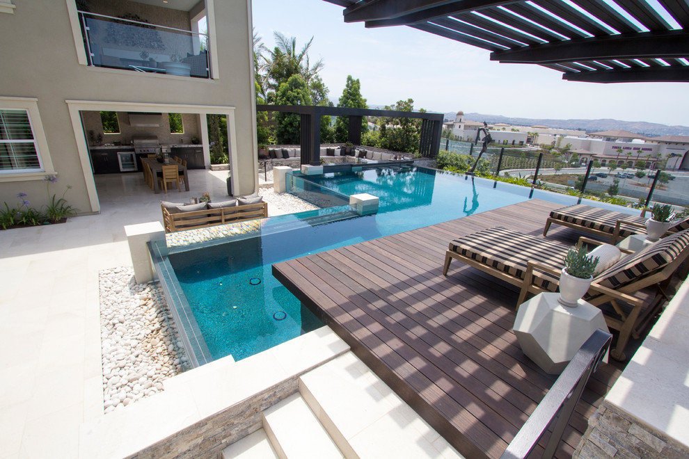 This is an example of a mid-sized modern backyard custom-shaped infinity pool in Orange County with a water feature and tile.