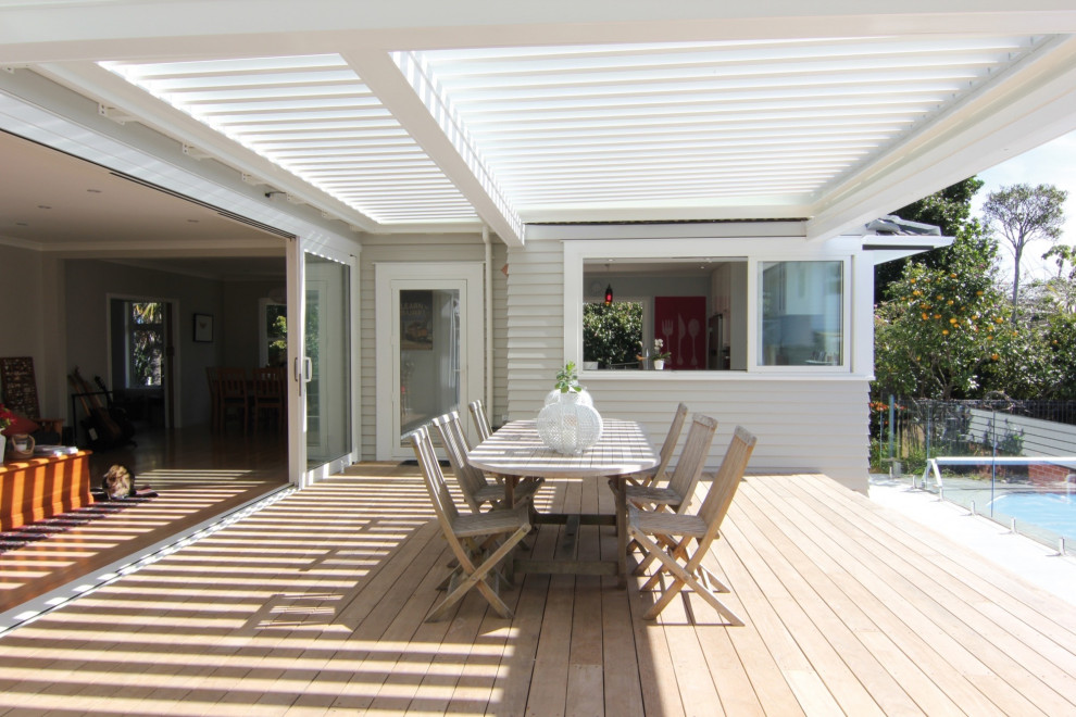 This is an example of a mid-sized modern backyard and ground level deck in Sydney with a pergola and glass railing.