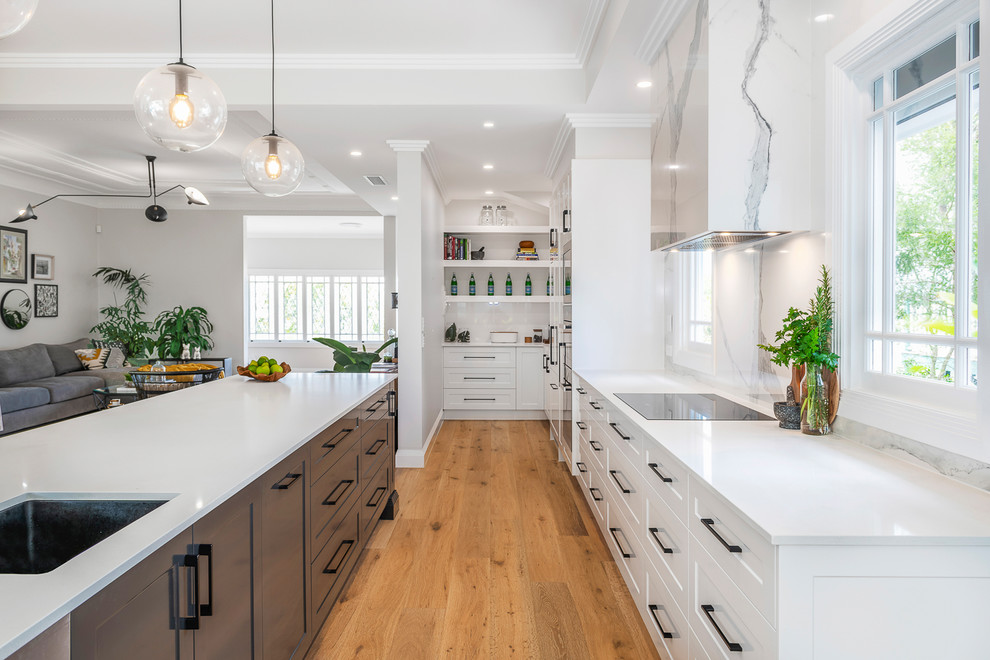 Photo of a large contemporary single-wall open plan kitchen in Brisbane with an undermount sink, shaker cabinets, grey cabinets, quartz benchtops, multi-coloured splashback, porcelain splashback, stainless steel appliances, light hardwood floors, with island and white benchtop.