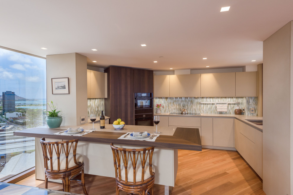 Small contemporary u-shaped eat-in kitchen in Hawaii with an undermount sink, flat-panel cabinets, beige cabinets, wood benchtops, multi-coloured splashback, glass tile splashback, black appliances, medium hardwood floors, a peninsula, brown floor and brown benchtop.