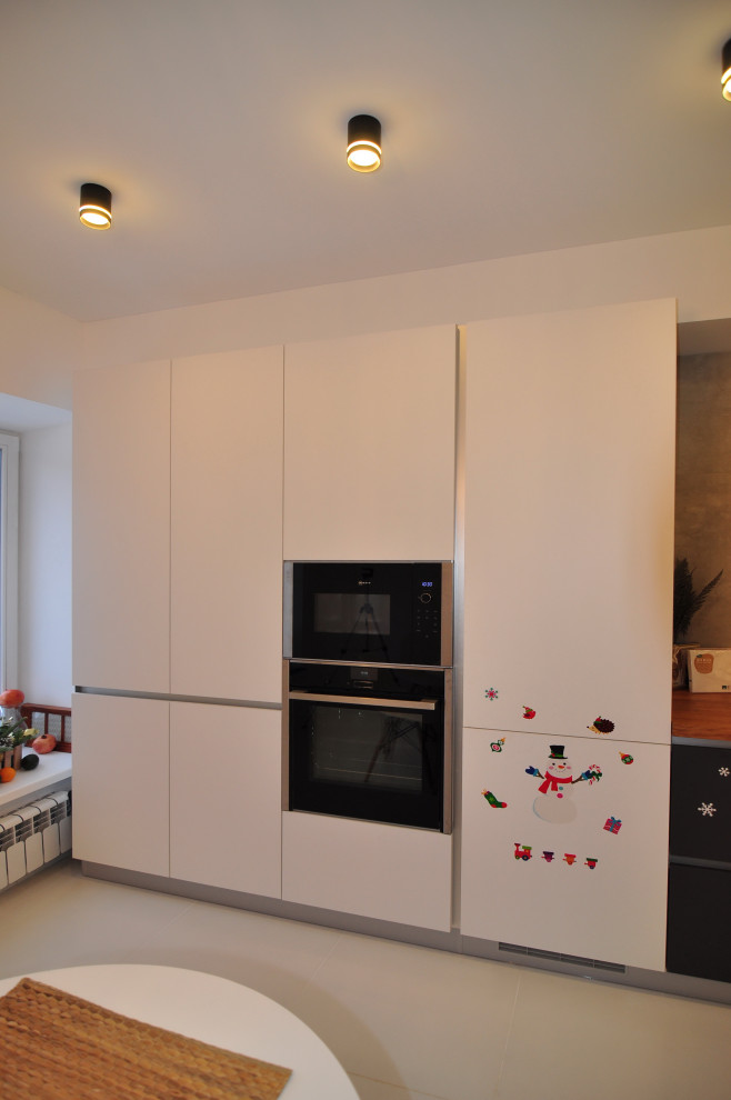 Photo of a large contemporary l-shaped eat-in kitchen in Other with an undermount sink, flat-panel cabinets, wood benchtops, white splashback, engineered quartz splashback, black appliances, porcelain floors, no island, white floor and beige benchtop.