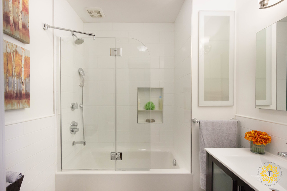 Design ideas for a mid-sized transitional bathroom in New York with an integrated sink, a shower/bathtub combo, a one-piece toilet, white walls, porcelain floors, glass-front cabinets, white tile, dark wood cabinets, a drop-in tub, porcelain tile and engineered quartz benchtops.