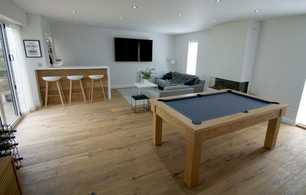 This is an example of a large scandinavian enclosed games room in West Midlands with a game room, white walls, medium hardwood flooring, a plastered fireplace surround and a wall mounted tv.
