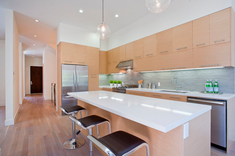 This is an example of a mid-sized contemporary l-shaped eat-in kitchen in San Francisco with an undermount sink, flat-panel cabinets, light wood cabinets, solid surface benchtops, grey splashback, matchstick tile splashback, stainless steel appliances, light hardwood floors and with island.