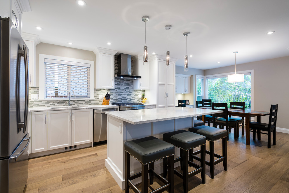 Open concept kitchen - mid-sized transitional l-shaped light wood floor and brown floor open concept kitchen idea in Vancouver with an undermount sink, shaker cabinets, white cabinets, quartz countertops, multicolored backsplash, mosaic tile backsplash, stainless steel appliances and an island