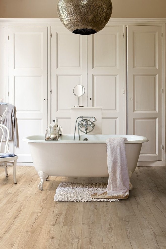 Photo of a traditional bathroom in London with raised-panel cabinets, white cabinets, a claw-foot tub, beige walls and light hardwood floors.