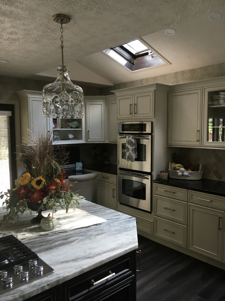 Large transitional u-shaped laminate floor and gray floor eat-in kitchen photo with an undermount sink, recessed-panel cabinets, white cabinets, granite countertops, white backsplash, ceramic backsplash, stainless steel appliances, an island and black countertops