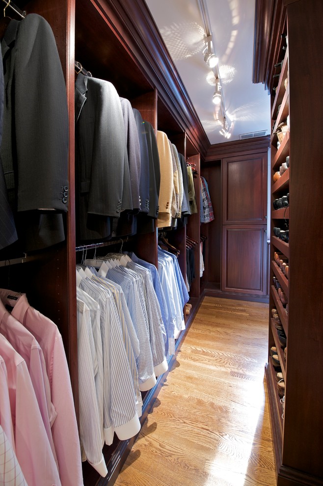 This is an example of an expansive traditional men's walk-in wardrobe in Philadelphia with raised-panel cabinets, dark wood cabinets and light hardwood floors.