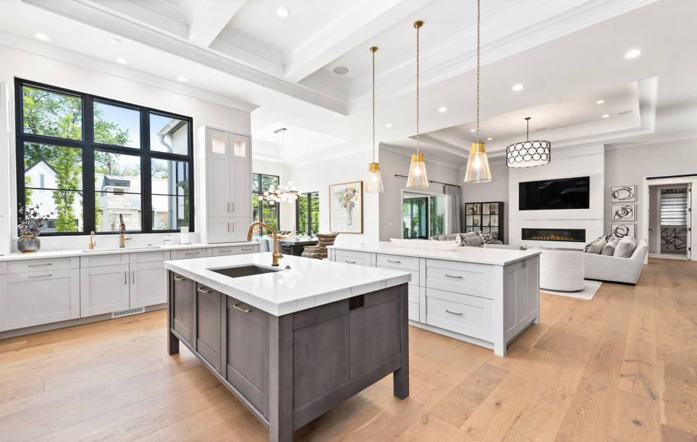 Photo of an expansive transitional u-shaped kitchen in Chicago with an undermount sink, shaker cabinets, grey cabinets, quartz benchtops, white splashback, engineered quartz splashback, stainless steel appliances, light hardwood floors, multiple islands, brown floor, white benchtop and coffered.