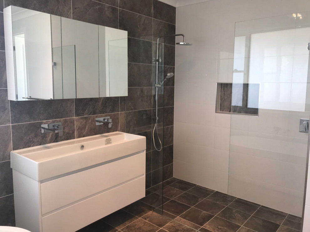 Photo of a large beach style master bathroom in Central Coast with furniture-like cabinets, white cabinets, a freestanding tub, a double shower, a one-piece toilet, gray tile, porcelain tile, white walls, porcelain floors, a trough sink, solid surface benchtops, grey floor, an open shower and white benchtops.