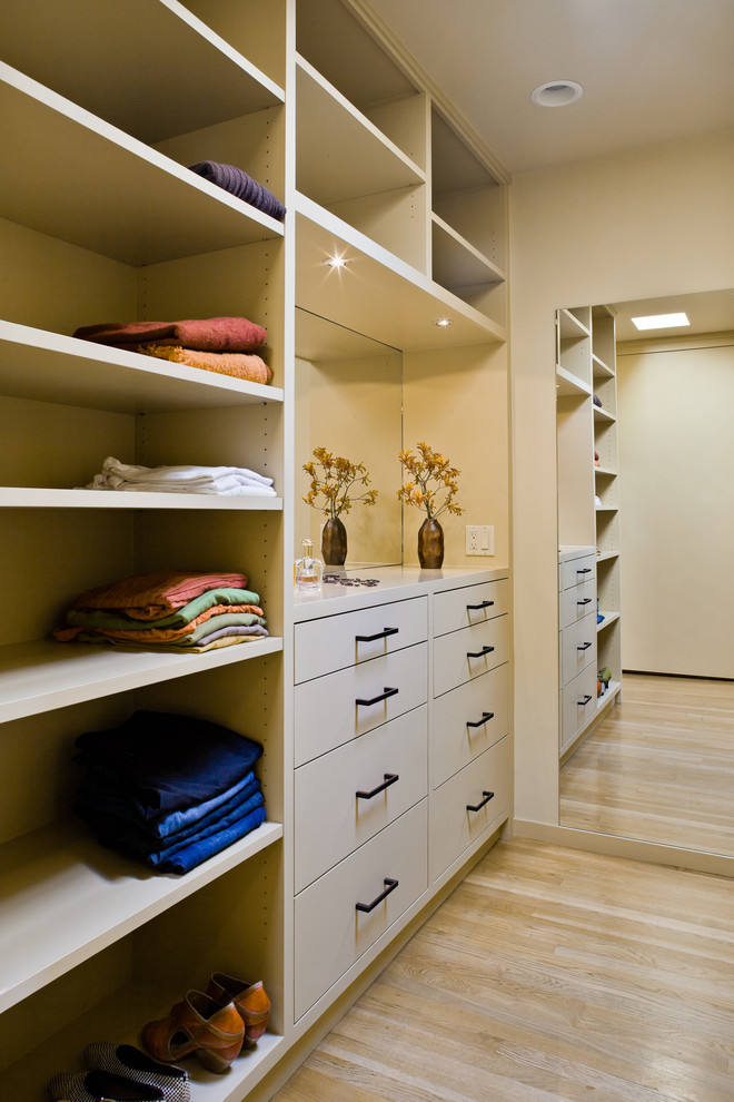 This is an example of a large modern walk-in wardrobe in San Francisco with flat-panel cabinets, beige cabinets and light hardwood floors.