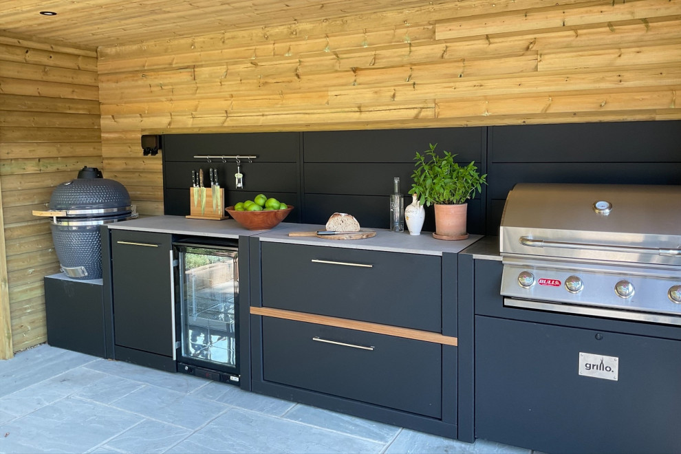 Réalisation d'une petite terrasse arrière design avec une cuisine d'été, des pavés en pierre naturelle et une pergola.