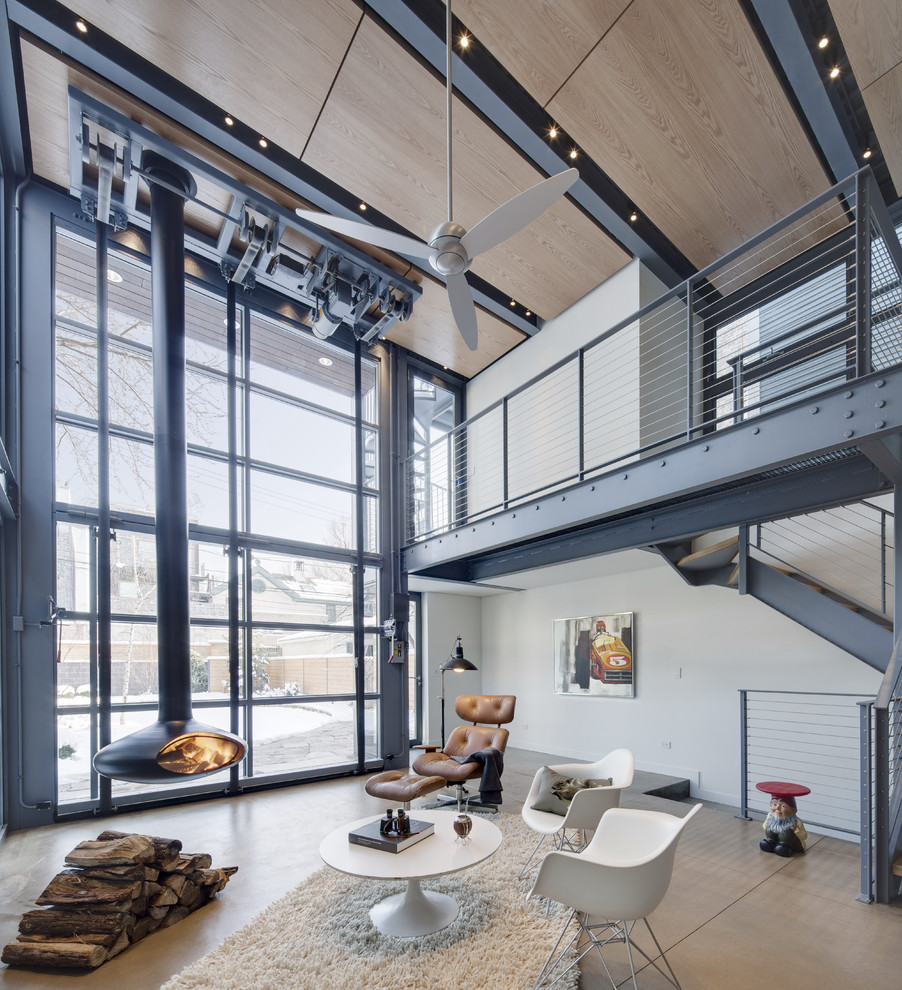 This is an example of a small industrial enclosed family room in Chicago with white walls, concrete floors and a hanging fireplace.