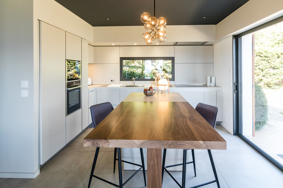 Photo of a mid-sized contemporary l-shaped open plan kitchen in Grenoble with a single-bowl sink, flat-panel cabinets, white cabinets, laminate benchtops, panelled appliances, with island, grey floor and white benchtop.