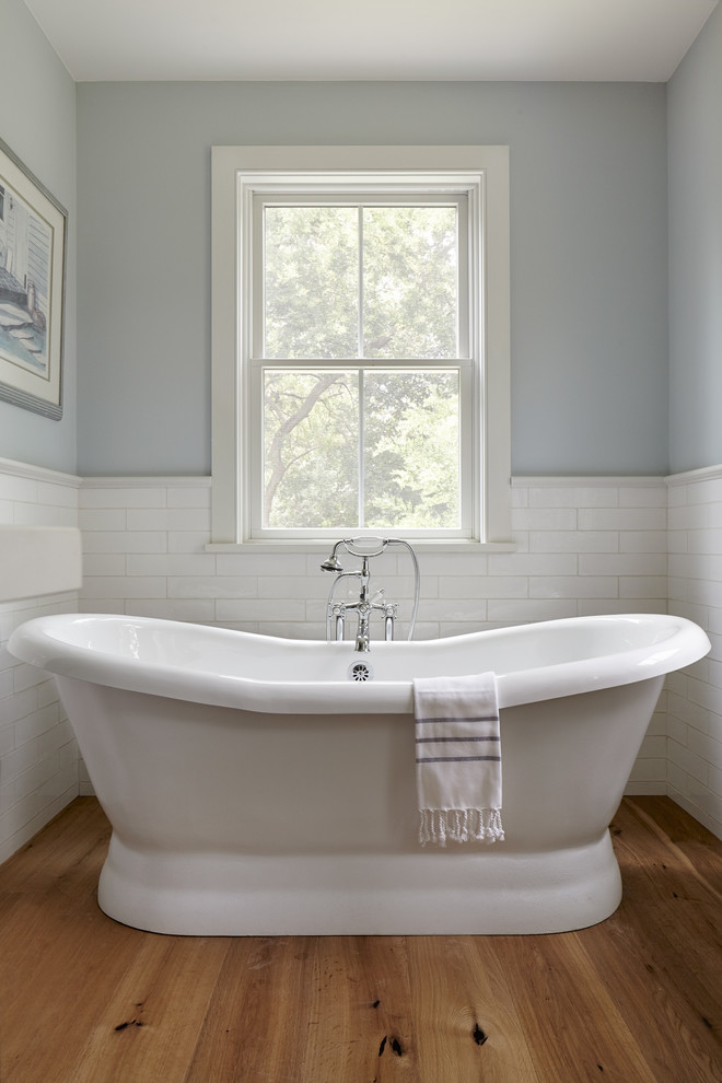 Inspiration for a mid-sized country master bathroom in Philadelphia with furniture-like cabinets, distressed cabinets, a freestanding tub, a two-piece toilet, white tile, ceramic tile, blue walls, light hardwood floors, an undermount sink, marble benchtops, brown floor and a hinged shower door.