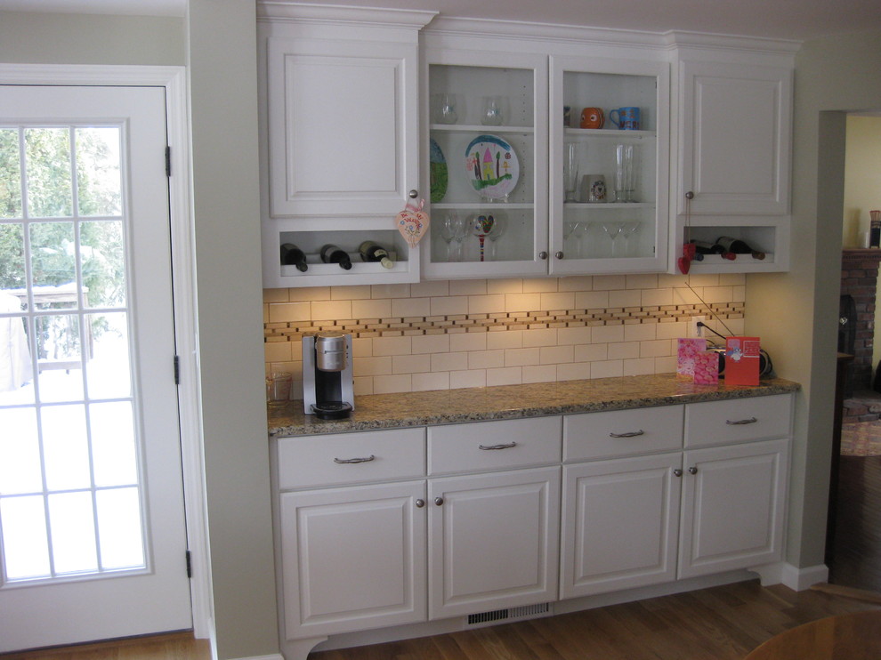 Inspiration for a transitional u-shaped medium tone wood floor eat-in kitchen remodel in Boston with an undermount sink, raised-panel cabinets, white cabinets, granite countertops, white backsplash, ceramic backsplash, stainless steel appliances, an island and beige countertops