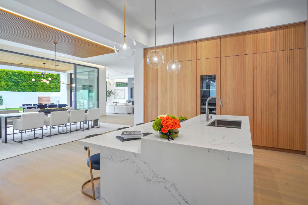 This is an example of an expansive modern u-shaped kitchen/diner in Los Angeles with a submerged sink, flat-panel cabinets, light wood cabinets, composite countertops, integrated appliances, light hardwood flooring, an island, white worktops and a wood ceiling.