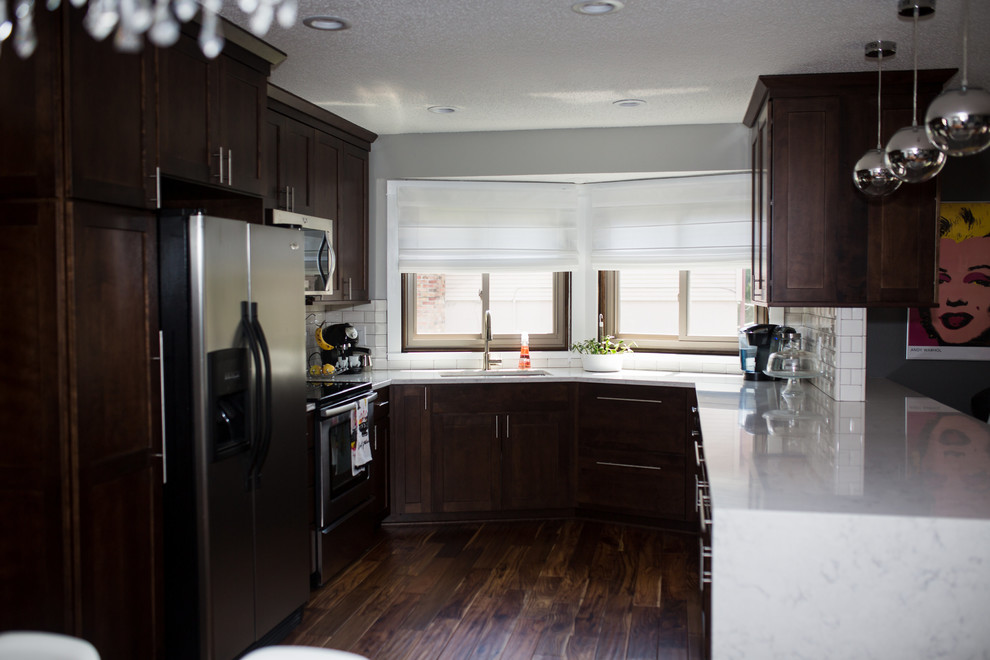 Example of a mid-sized transitional u-shaped medium tone wood floor and brown floor enclosed kitchen design in Omaha with an undermount sink, shaker cabinets, dark wood cabinets, quartz countertops, white backsplash, subway tile backsplash, stainless steel appliances and a peninsula