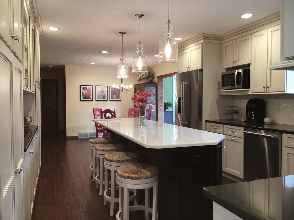Large transitional medium tone wood floor and brown floor eat-in kitchen photo with an undermount sink, flat-panel cabinets, white cabinets, granite countertops, white backsplash, porcelain backsplash, stainless steel appliances and an island
