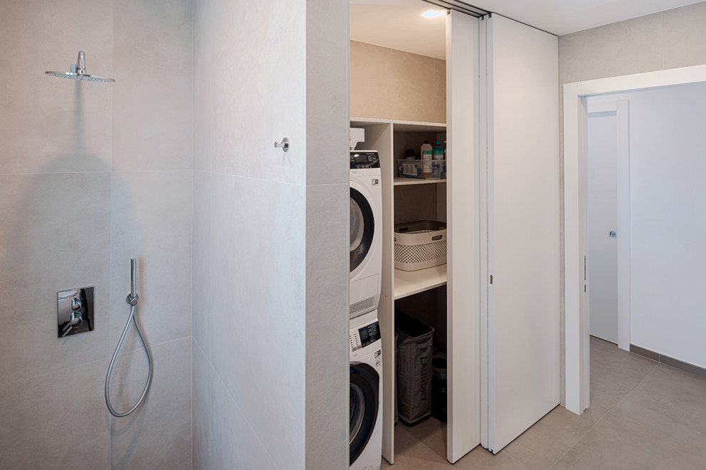 Photo of a small contemporary single-wall dedicated laundry room in Naples with open cabinets, white cabinets, laminate benchtops, grey splashback, porcelain splashback, grey walls, porcelain floors, a stacked washer and dryer, grey floor and white benchtop.