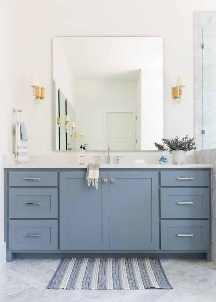 This is an example of a large traditional master bathroom in Dallas with shaker cabinets, blue cabinets, a freestanding tub, a corner shower, gray tile, marble, grey walls, marble floors, an undermount sink, engineered quartz benchtops, grey floor, a hinged shower door and white benchtops.