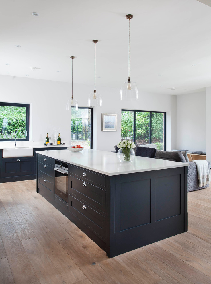 Mid-sized country single-wall eat-in kitchen in Belfast with a farmhouse sink, shaker cabinets, grey cabinets, quartzite benchtops, metallic splashback, glass sheet splashback, stainless steel appliances, medium hardwood floors and with island.