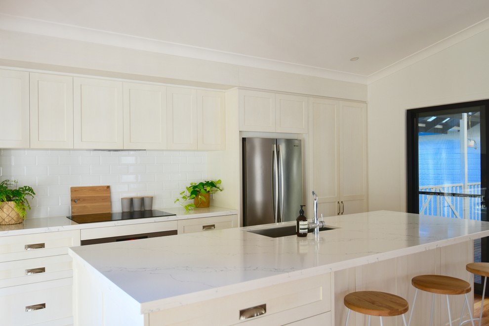 Photo of a modern kitchen pantry in Sunshine Coast with a farmhouse sink, shaker cabinets, white cabinets, quartz benchtops, white splashback, subway tile splashback, stainless steel appliances, medium hardwood floors and with island.