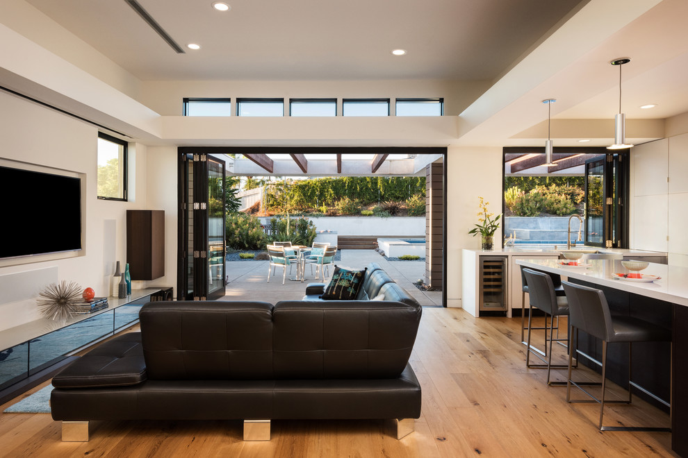This is an example of a contemporary formal open concept living room in San Diego with beige walls, medium hardwood floors, a wall-mounted tv and beige floor.