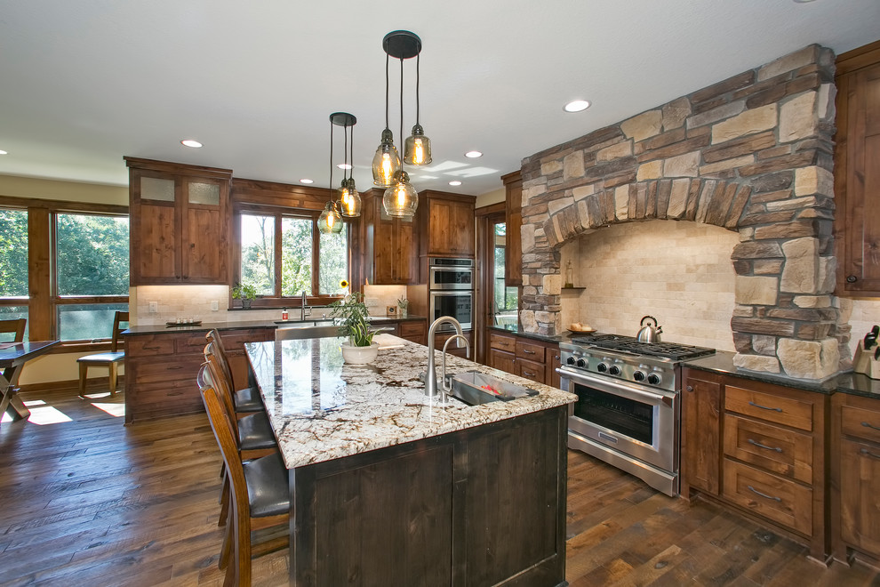 Photo of a country l-shaped kitchen in Minneapolis with a farmhouse sink, shaker cabinets, dark wood cabinets, beige splashback, stainless steel appliances, dark hardwood floors, with island, brown floor and black benchtop.