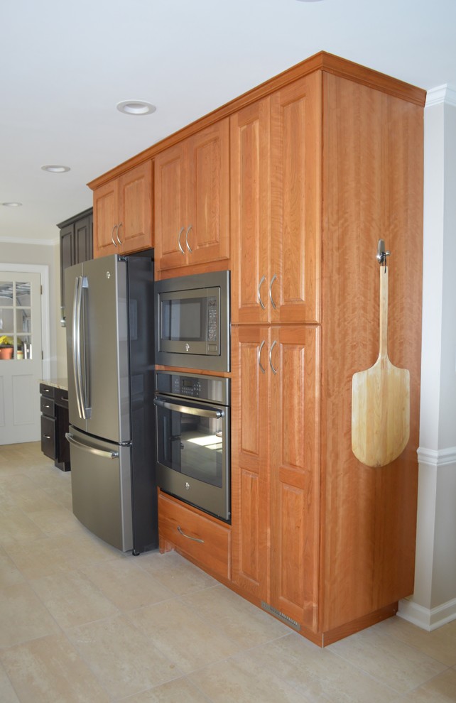 Example of a large transitional l-shaped porcelain tile and beige floor eat-in kitchen design with a farmhouse sink, raised-panel cabinets, brown cabinets, granite countertops, white backsplash, ceramic backsplash, stainless steel appliances and a peninsula